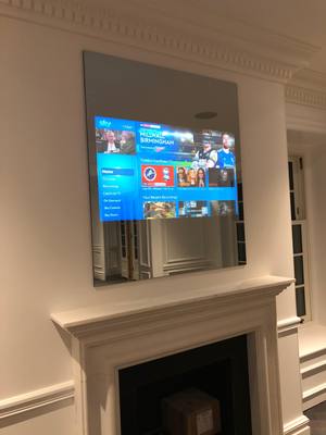 Hidden mirror TV installation above a fireplace with Sky TV display